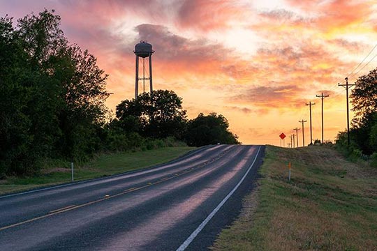A rural road with trees on the sides at sunset.