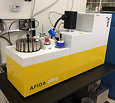 A photo of a yellow and white piece of table-top equipment with various holders and other mechanisms on top of it.