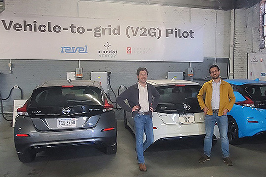 Two people standing in a garage with electric vehicles.