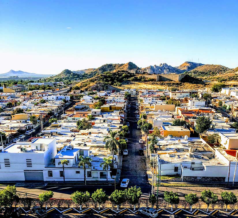Photo of a neighborhood with houses, trees, and small mountains in the background.