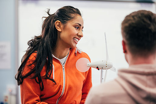 Person smiling in front of model wind turbine while another person looks at it.