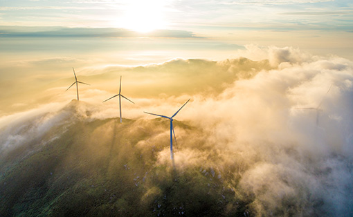 Wind turbines peak out of clouds in sunrise sky.