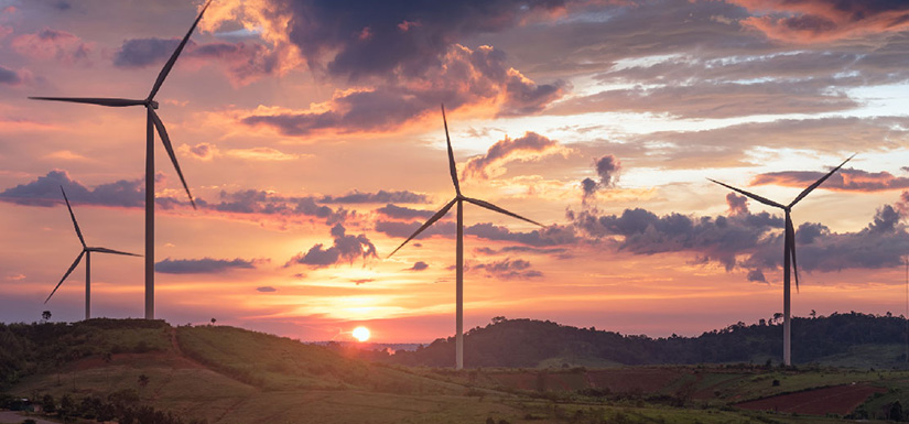 Wind turbine in a field at sunset with cloudy skies overhead.