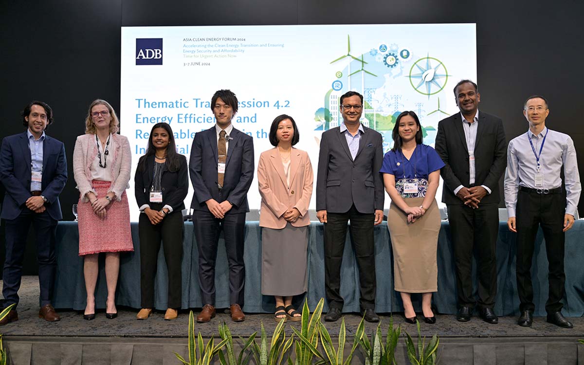 A group of nine individuals smiling and posed for a photo in front of a panel table and background.