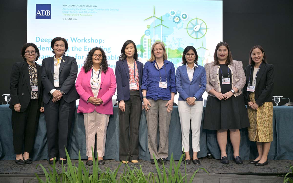 A group of eight women smiling and posing for a photo in front of a panel table and background