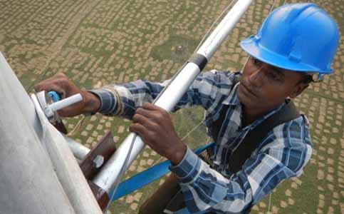 A man in a hardhat installs a sensor on a tower high above the ground.