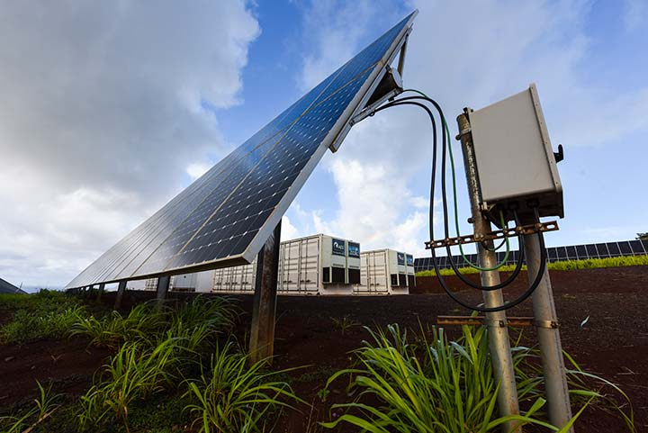 Solar panels in a green field with large-scale battery storage situated behind the panels.