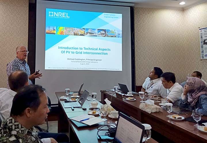 A man presents a PowerPoint in front of a group of people in a conference room