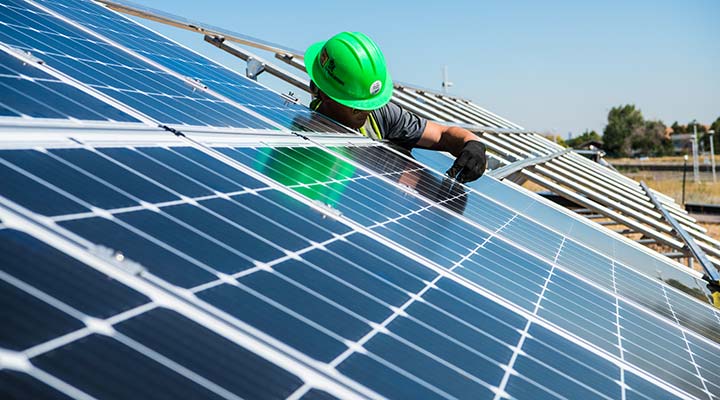 A worker in a hardhat installing a solar panel.