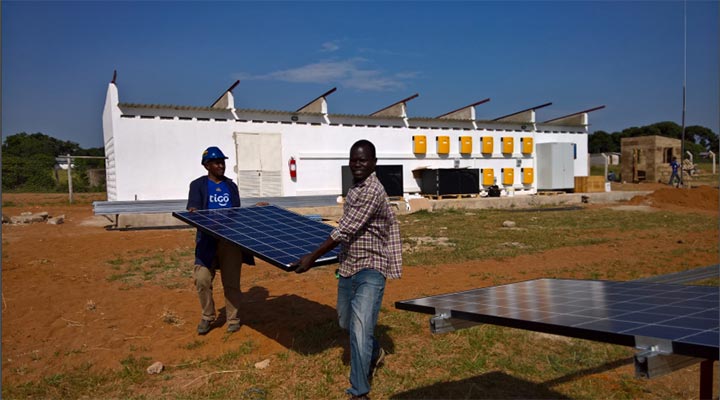 Two men carry a solar panel to place on an array assembly.