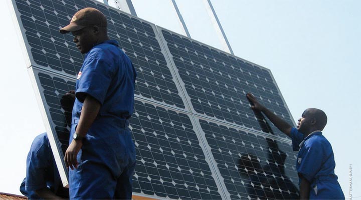 Two men support a solar panel being installed on a microgrid, while two others work behind it.