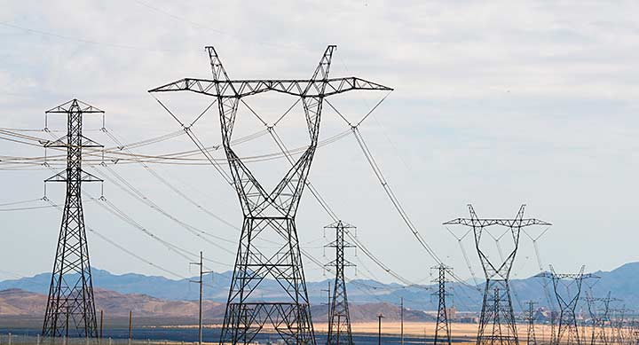 Transmission pylons and lines stretching across a flat landscape with mountains in the background.