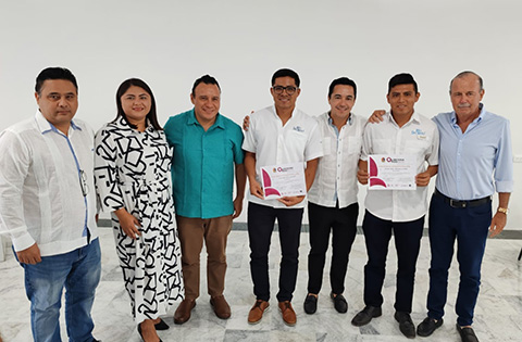 A group of seven people pose together in a row. Two of them are holding certificates.