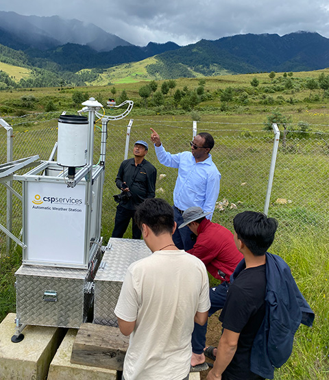 Manajit Sengupta and Aron Habte of NREL help a group of Druk Green Power Corporation staff in leveling of solar resource measurement instruments near Bhumtang Bhutan. There are mountains and clouds in the distance.