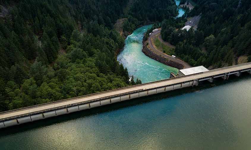 A dam at the edge of a reservoir releases a river through a forest