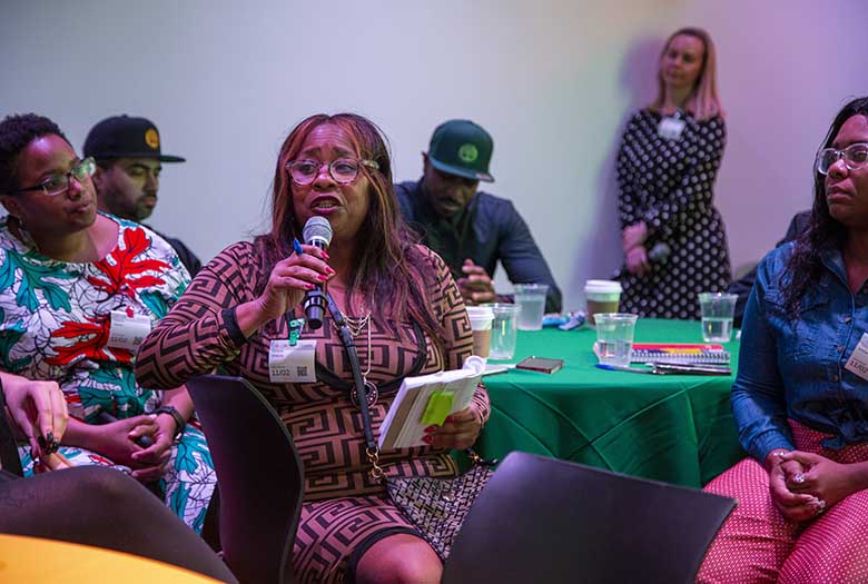 Diverse people sitting at a table, where one speaks into a microphone.