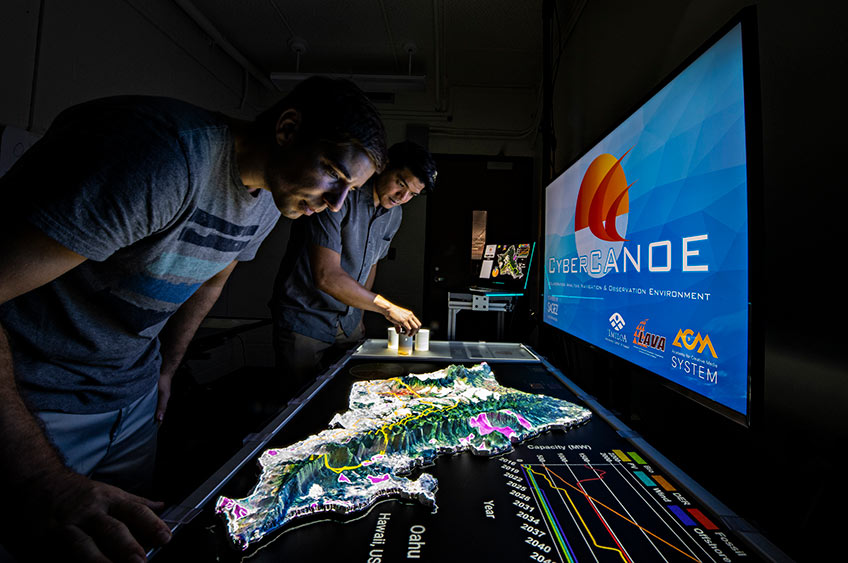 Photo of two researchers at a computer looking at a 3-D rendering of data.