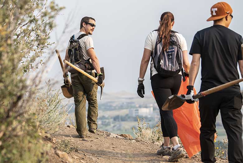 A man with shovel and pickaxe walks on a trail.