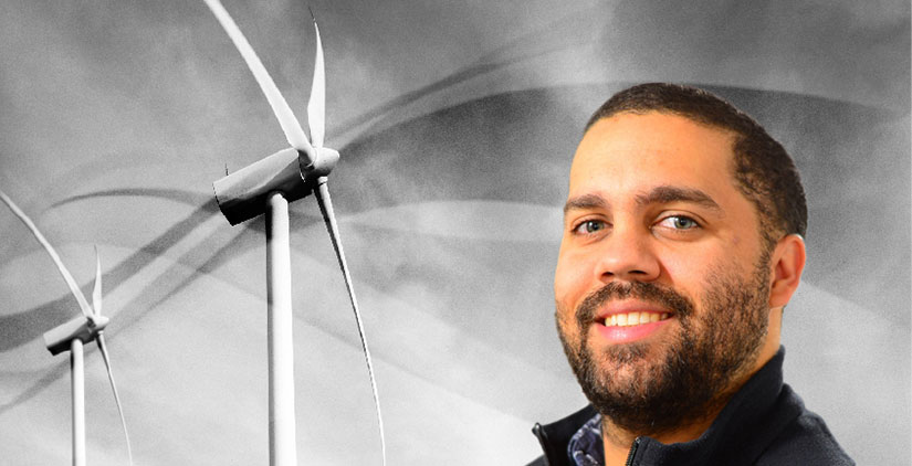A headshot of Cory Frontin in front of two wind turbines