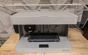  A gray device sits on a table. The interior is hollow except for a few mechanisms and a black platform.