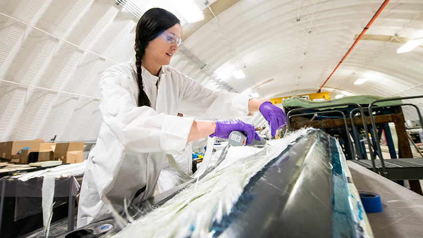 A researcher wearing a white coat, safety goggles, and purple gloves works in a white, half-dome facility.
