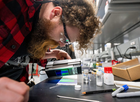 A person holds a digital instrument over objects on a table that holds vials containing different materials.