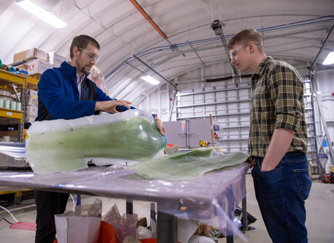 Two people standing over a table, one handling a large object encased in plastic.