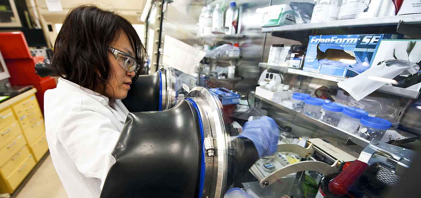 A woman in a lab coat works in a laboratory assembling a lithium Ion battery.
